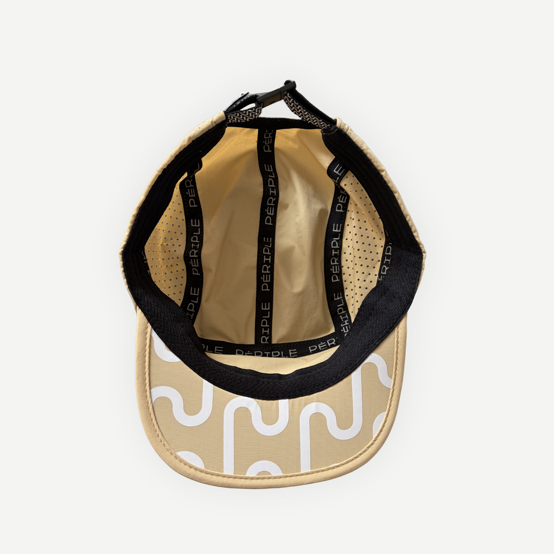 Intérieur de la casquette de course beige Périple montrant les coutures renforcées, la bande de confort et l'imprimé graphique signature visible sous la visière.