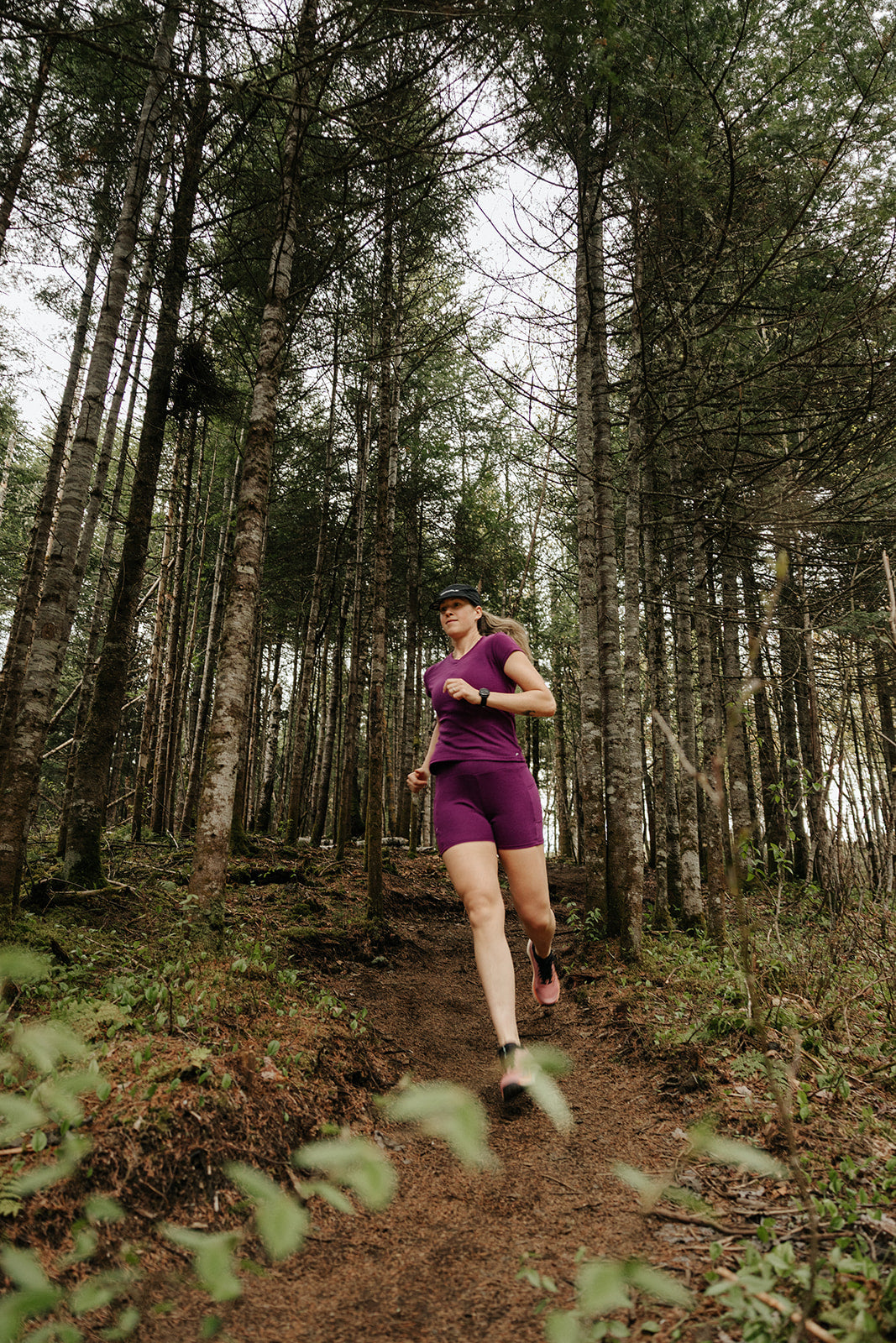 Femme portant un biker short et un t-shirt col V en laine de mérinos pourpre lors d'une course en sentier en forêt.