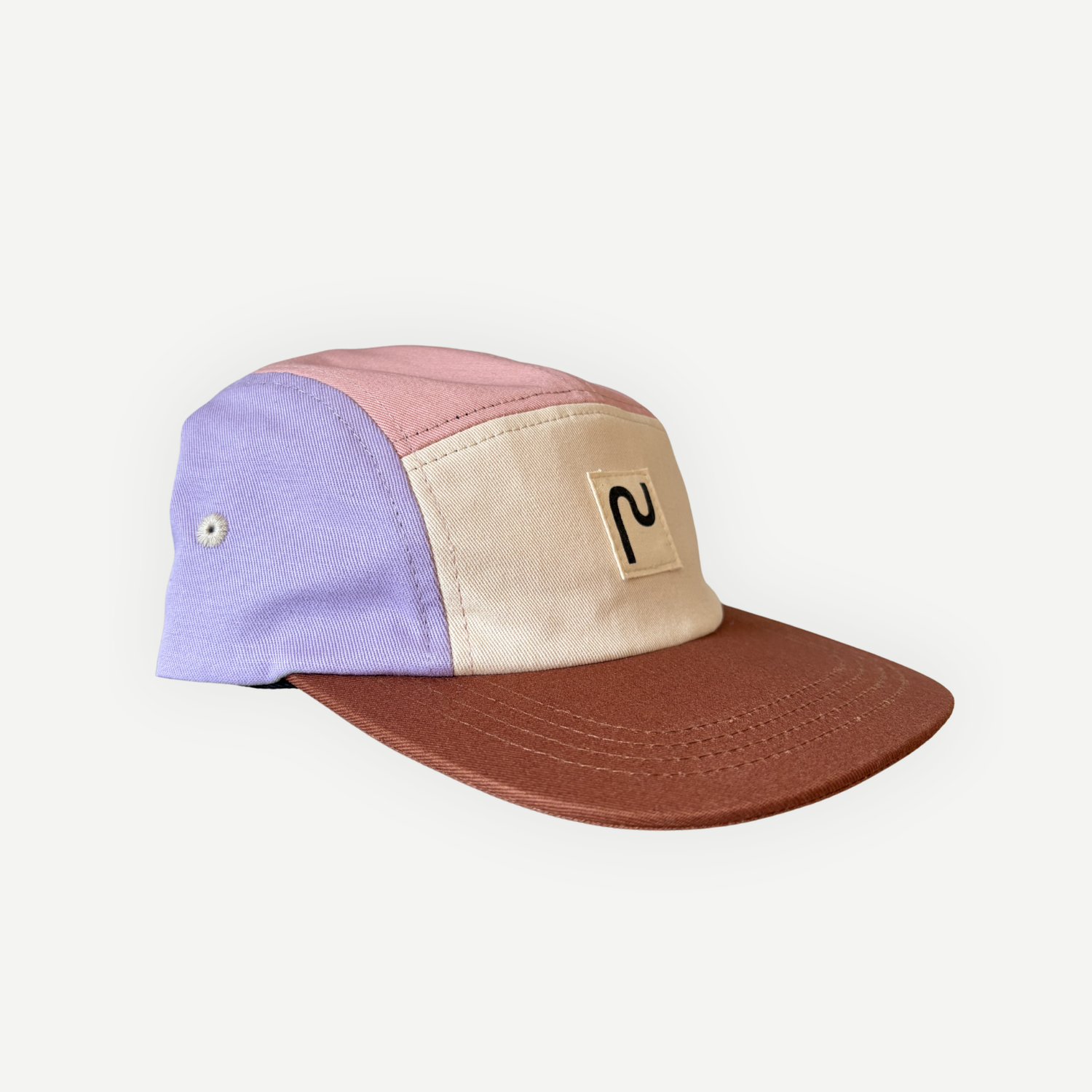 Casquette en coton à 5 panneaux de la marque Périple. Modèle colorblock lila, rose, jaune moutarde et crème avec visière brun cacao, vue latérale gauche.