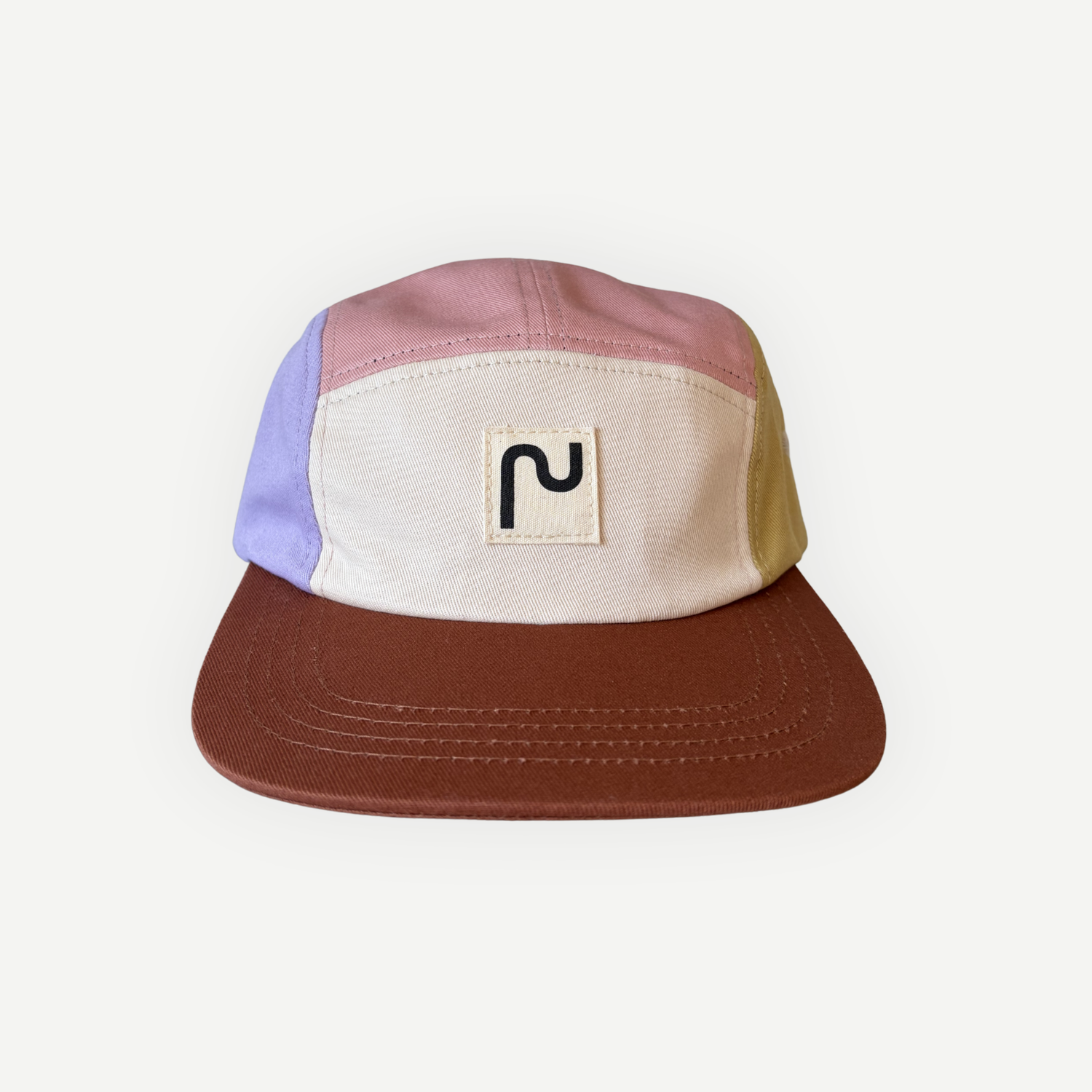 Casquette en coton à 5 panneaux de la marque Périple. Modèle colorblock lila, rose, jaune moutarde et crème avec visière brun cacao, vue de face.