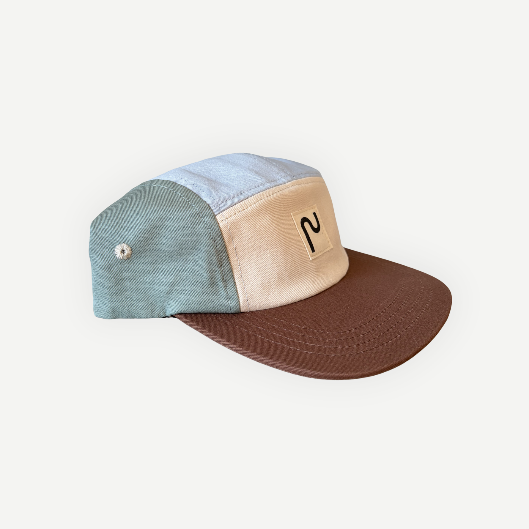 Casquette en coton à 5 panneaux de la marque Périple. Modèle colorblock sauge marine et crème avec visière brun cacao, vue latérale gauche.