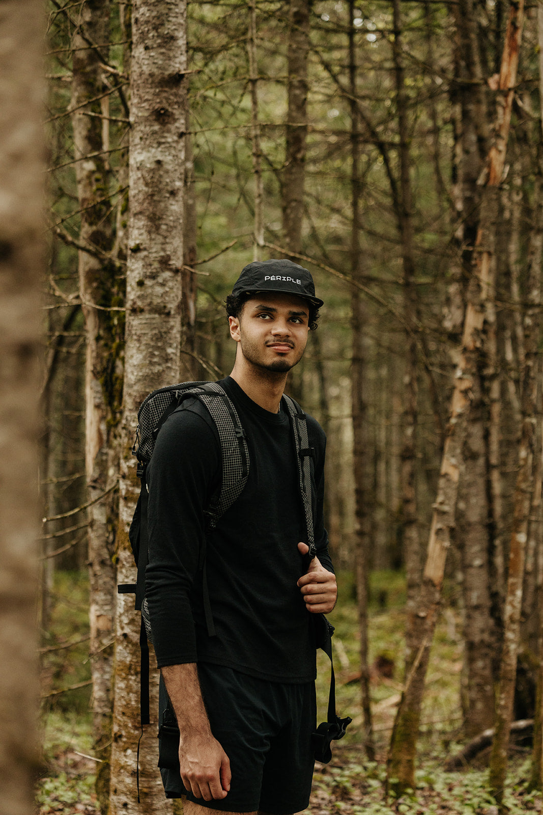 Homme portant le chandail en laine de mérinos à manches longues ainsi que la casquette de course Périple noir lors d'une randonnée en forêt. 