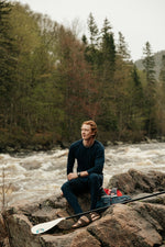 Homme avec une veste de flottaison et une pagaie sur le bord d'une rivière portant le chandail à manches longues pour homme marine ainsi que le caleçon en laine de mérinos marine. 