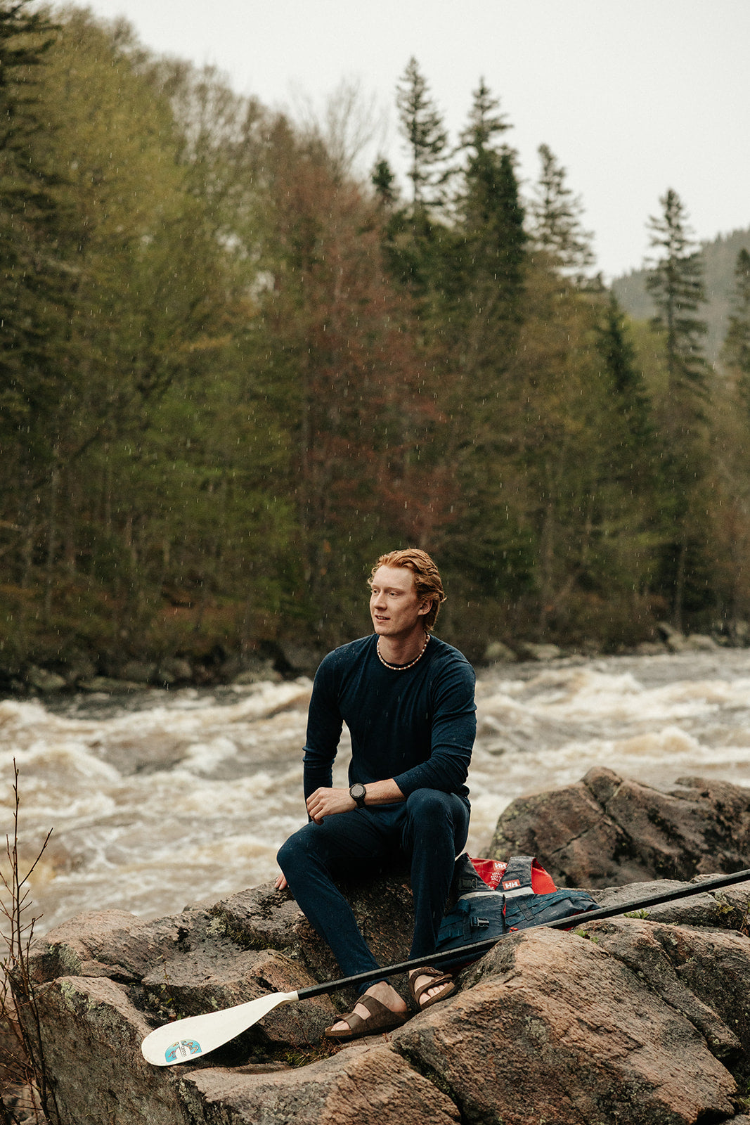 Homme avec une veste de flottaison et une pagaie sur le bord d'une rivière portant le chandail à manches longues pour homme marine ainsi que le caleçon en laine de mérinos marine. 