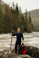 Homme avec une pagaie et une veste de flottaison tout près d'une rivière. Il porte le chandail à manches longues en laine de mérinos marine ainsi que le caleçon en laine de mérinos marine. 