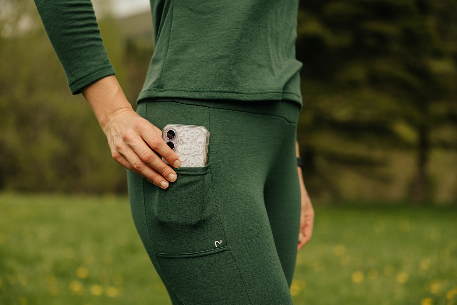 Gros plan sur la poche latérale du legging thermique en laine de mérinos Émeraude pour femme, avec téléphone rangé lors d'une randonnée.