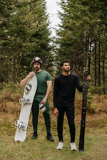 Hommes portant les sous-vêtement thermique en laine de mérinos, dont le t-shirt Émeraude et le chandail Ardoise avec un snowboard et des skis.