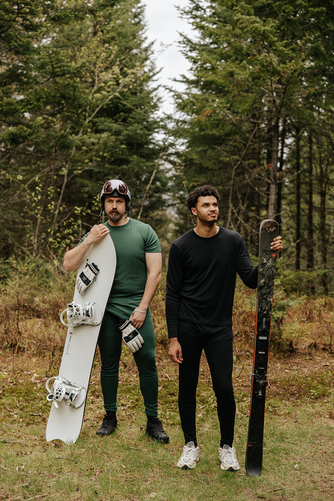 Hommes portant les sous-vêtement thermique en laine de mérinos, dont le t-shirt Émeraude et le chandail Ardoise avec un snowboard et des skis.