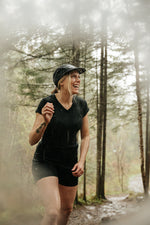 Femme portant un t-shirt col V et un biker short en laine de mérinos Ardoise lors d'une randonnée sous la pluie en forêt.